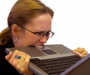 An angry woman holding up a laptop computer to her face and biting it.