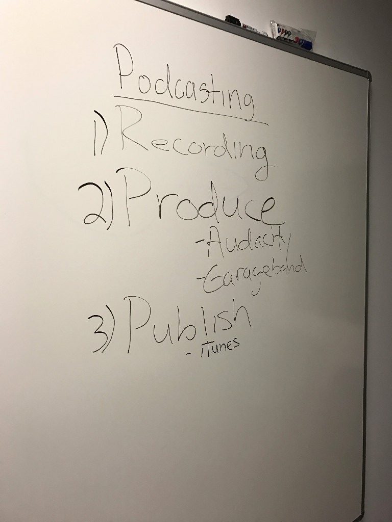 a whiteboard with text written in black marker. we are viewing from an off angle. the text readings "Podcasting: 1) Recordings, 2) Produce - Audacity - Garageband, 3) Publish - iTunes