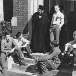 Father John Delaunay standing on the front steps of Christie Hall surrounded by a group of students.