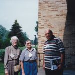 Three people standing outside in front of a brick building.
