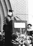 Father David Sherrer standing on stage at a lectern while wearing academic regalia.