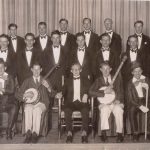 Group of people wearing tuxedos and hat and bow ties.