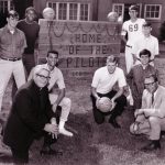 Father John Van Wolvlear and basketball players around the Home of the Pilots sign outside Howard Hall.