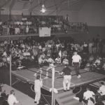 Spectators watching a boxing match in a gymnasium arena.