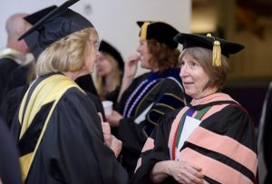 Doctor Susan Stillwell facing Jane Scott, both wearing academic regalia.