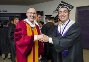 Doctor Michael Connolly congratulates a University of Portland graduate, both are dressed in academic regalia.