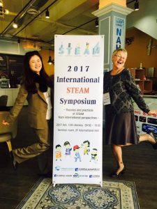 Doctor Tisha Morell (right) next to the 2017 International STEAM Symposium sign.