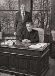 Doctor Arthur Schulte standing next to Father David Tyson seated at his desk.