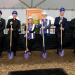 Six individuals wearing hard hats and holding shovels for a groundbreaking ceremony.