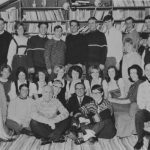 Group of college students dressed in sweathers or traditional German clothing posed in front of bookshelves.