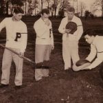 Group of four students in letter sweaters with a P on the front, one holding a shovel over a newly dug hole in the ground while another places a football into the hole.