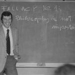 Man standing at a chalkboard with the words Fallacy No. 1: Philosophy is not important written on the chalkboard.