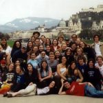 Group of college students posed with Fortress Hohensalzburg and the city of Salzburg, Austria behind them.