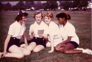 four girls sitting on the grass, one is wearing a beanie cap