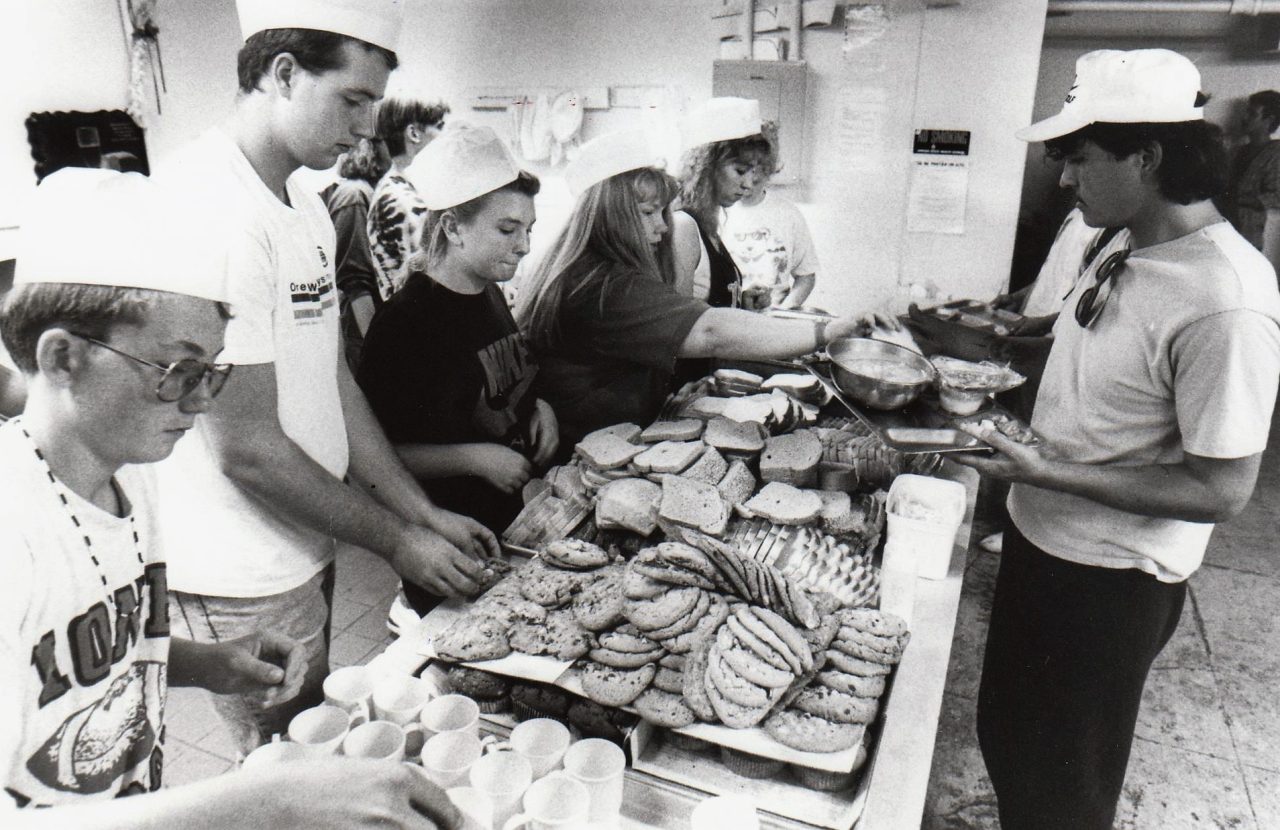 Student volunteers serve bread and cookies in a food buffet line.