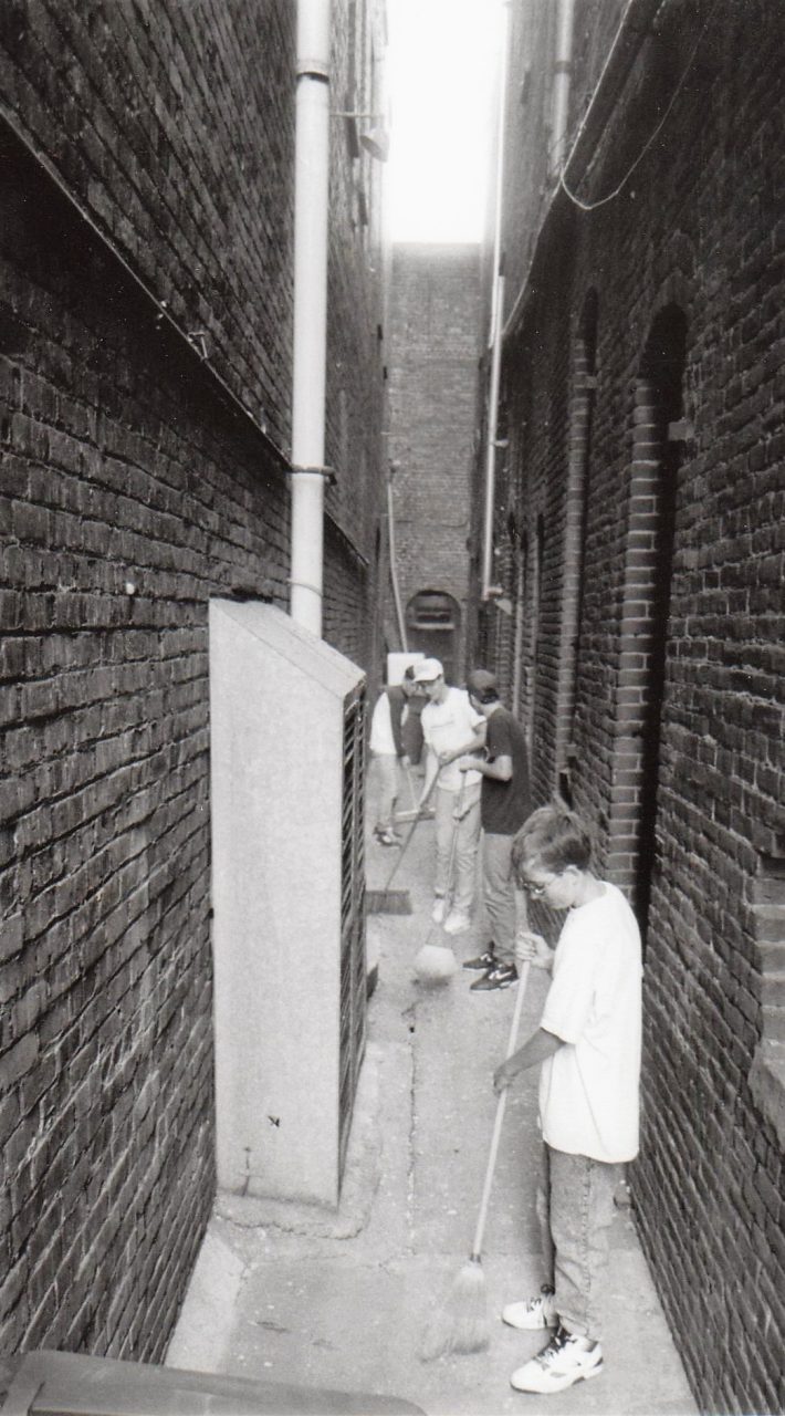 Volunteers sweep a narrow alleyway between buildings.