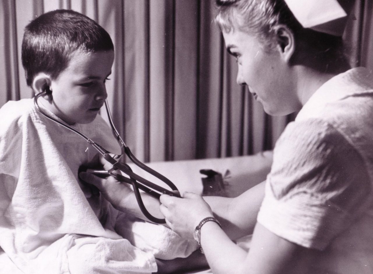 Nurse helping a young boy wearing a stethoscope listen to his own heart