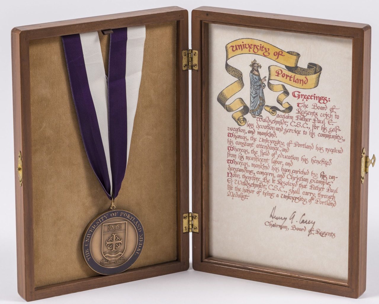 Medal attached to a purple and white ribbon, descriptive text, and recipient Father Paul E. Waldschmidt.